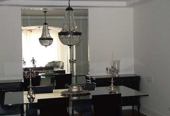 clássica sala de jantar com móveis pretos, espelho, mesa de vidro e luxuoso lustre