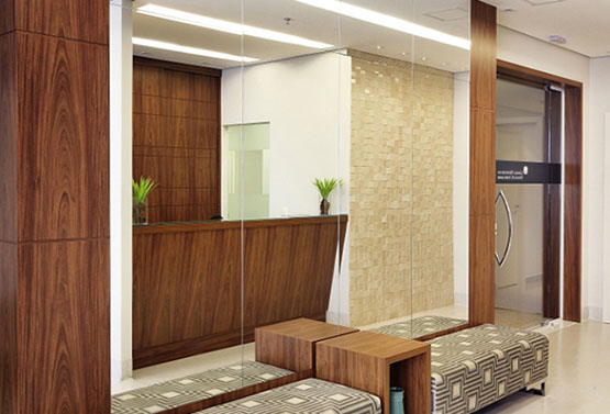sala de espera com espelho na parede, bancos acolchuados e porta de vidro